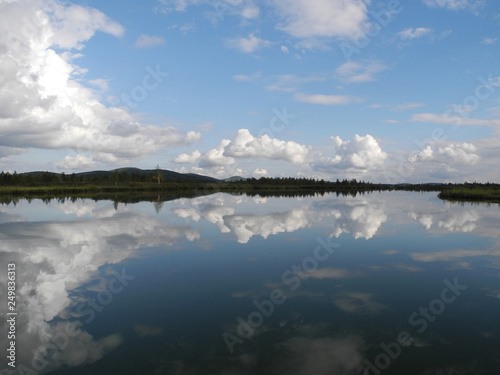 Reflection of blue sky with white clouds in calm still water of a mountain lake