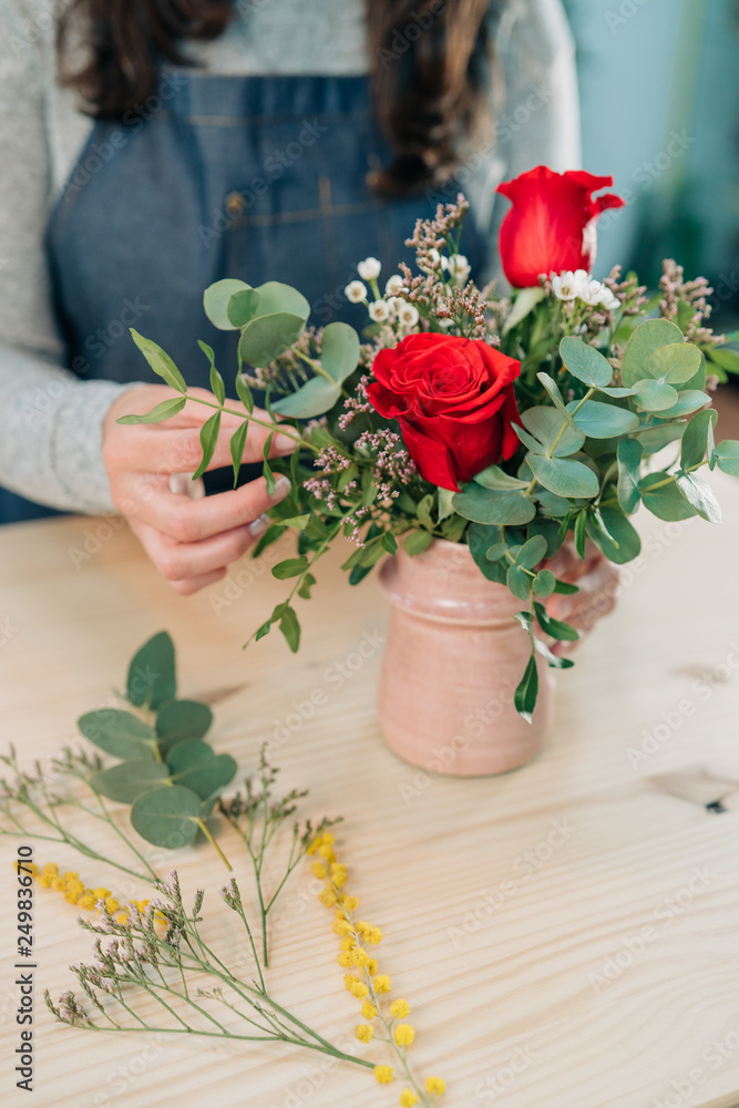 Woman florist makes a red roses bouquet on wooden table