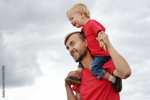 Touching family moments. Cute toddler boy sitting on his father's shoulders. They are smiling, laughing and looking happy. Parenthood or childhood concept