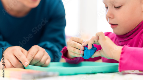 Toddler girl in child occupational therapy session doing sensory playful exercises with her therapist. photo
