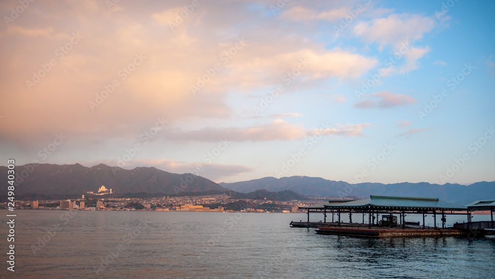 Landscape photo of the beautiful view that can be seen right outside the West Japan Railway Miyajima Ferry Terminal with the jetty in view, during the early morning, with dramatic clouds in the sky.