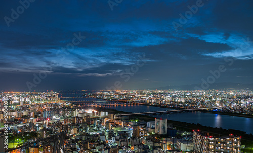 Panoramic, scenic view of Japan's Osaka city from the observatory deck of Umeda Sky Building during sunset with dramatic clouds in the blue and orange sky.