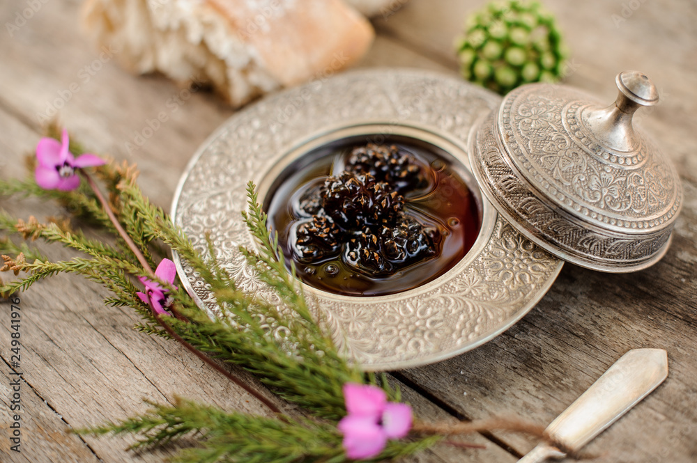 Cones jam in the silver plate with a cap, tree branch with a pink flowers and bread near it