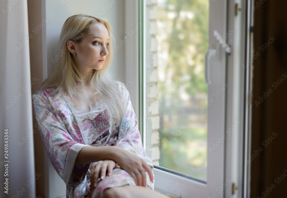 Pensive girl in bathrobe sitting on the windowsill. Natural light.