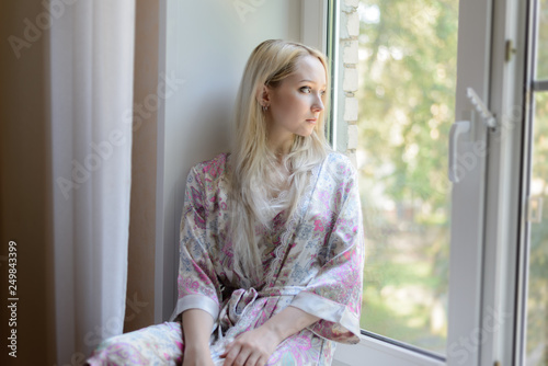 Pensive girl in bathrobe sitting on the windowsill. Natural light. © Vladimir Arndt