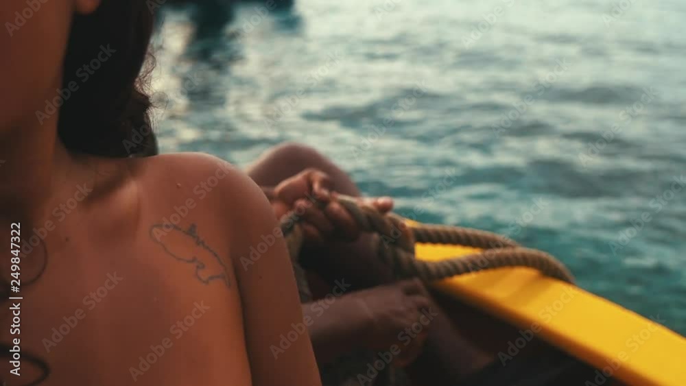 Fisherman tightening rope on his boat behind a girl with a Martinique tatoo on her shoulder
