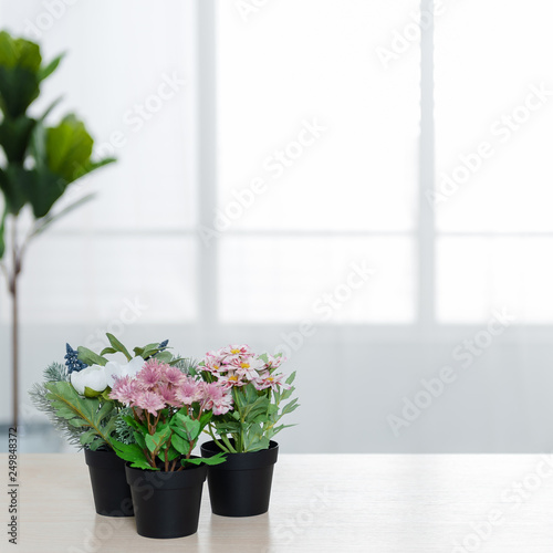 There are beautiful flowers and various objects in front of big living room windows.