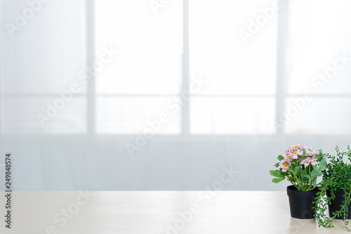 There are beautiful flowers and various objects in front of big living room windows.