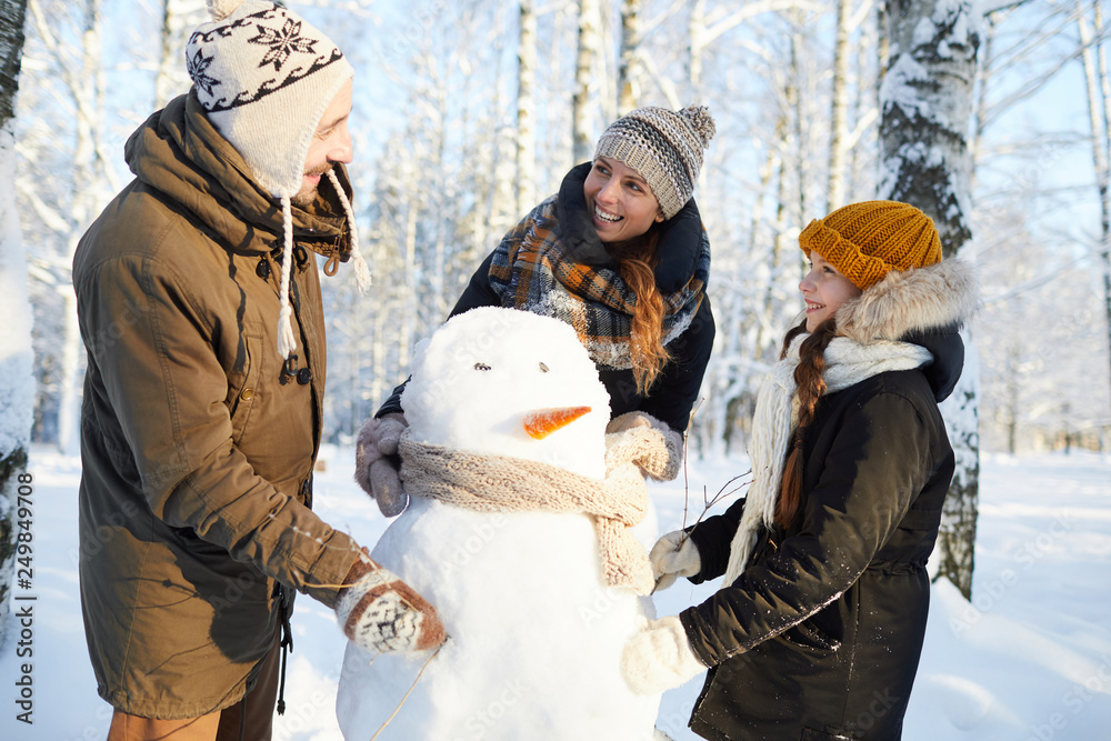 Portrait of happy family building snowman in winter forest and laughing, copy space