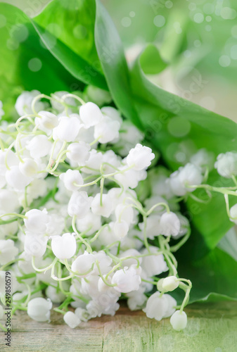 Spring white fragrant lilies of the valley in bouquet with leaves on vintage wooden table, selective focus