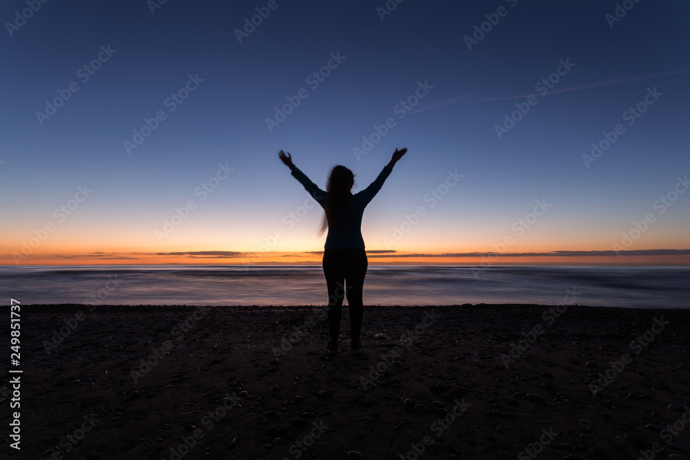 Freedom, holiday and victory concept - Silhouette of woman with hands up while standing on the sea beach at sunset
