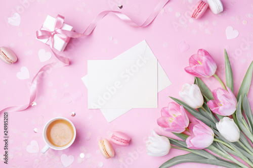 Morning cup of coffee, cake macaron, gift box, envelope and spring tulip flowers on pink background. Beautiful breakfast for Women day, Mother day. Flat lay.