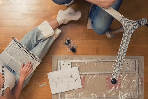 Man and woman assembling furniture on wooden parquet using instruction for for self assembly