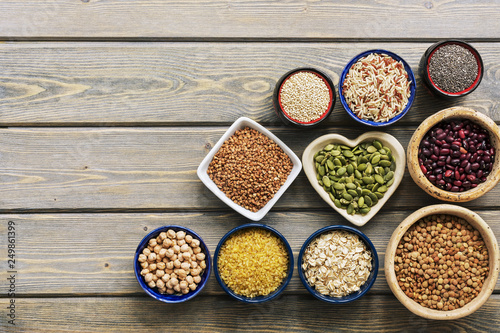 A set of various superfoods — whole grains,beans, seeds, legumes in bowls on a wooden plank table. Top view, copy space.