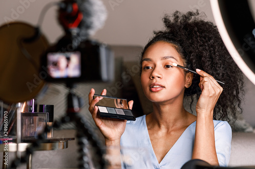 Foto Female video blogger applying make up on face in living room