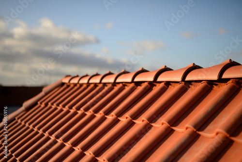 Dachfirst und glänzend rote Dachziegel Pfannen vom Dachdecker im Sonnenschein vor  dunklem Hintergrund photo
