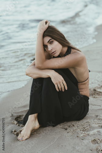 Beautiful thoughtful woman with golden frackles sitting on the beach photo