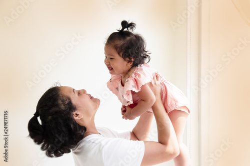 Mother raising her daughter up in the air with smile and happy face Mother-child bond blurry light around
