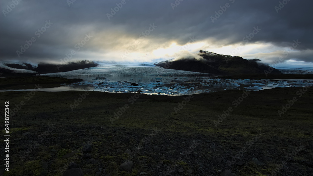 Fjallsarlon glacial lagoon with floating icebergs and glacier and mountains behind with overcast sky. Southern Iceland.