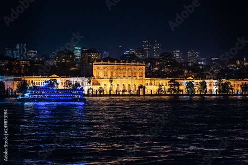 View of the Dolmabahche palace in beams of night-time lighting. Skyscrapers of modern Istanbul at a background and sea ferry on front side is visible. photo