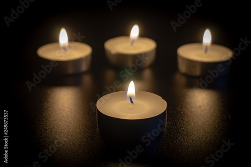 Four tea candles with reflection on black