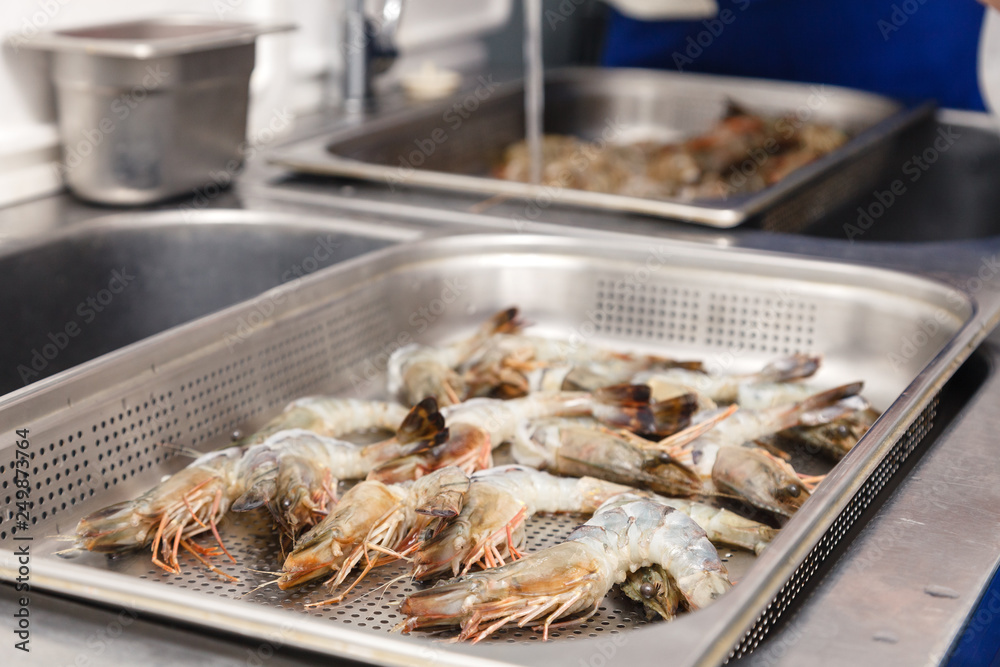 Closeup fresh royal raw shrimps with heads on professional perforated gastronorm container in sink are ready to be baked in the oven in staurant's kitchen. Concept preparation for seafood dish