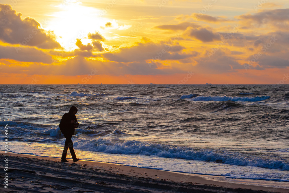 Naklejka premium silhouette of a man walking along the beach during a bright sunset