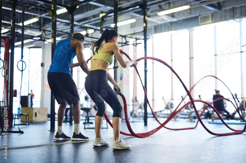 Fotografia Back view of intercultural man and woman in activewear practicing rope battle in