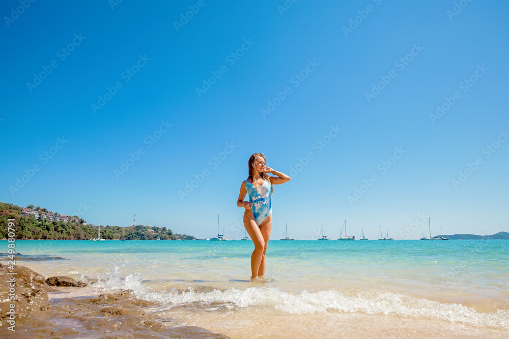 Beautiful young woman with long hair in a blue swimsuit standing in the sea and relax on the beach on Phuket, Thailand