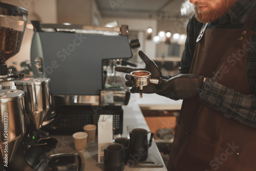 Barista holding a holder with ground coffee and ready for preparing coffee for a professional coffee machine. Bartender prepares coffee  holding a portafilter in hands. Coffee concept