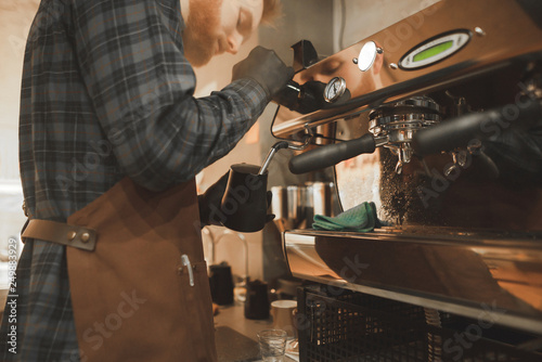 Close-up barista photo of steaming milk for coffee on a professional coffee machine. Barista's husband warmes the milk in pitcher. Barista in the process of creating cappuccino.