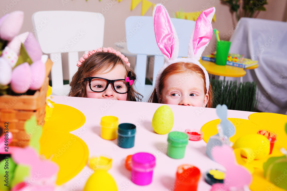 children in the rabbit's ears peek out from under the table on the background of the Easter decor. Preparation for the celebration of Easter. Hunting for the Easter Bunny children in the rabbit's ears peek out from under the table on the background of the Easter decor. Preparation for the celebration of Easter. Hunting for the Easter Bunny