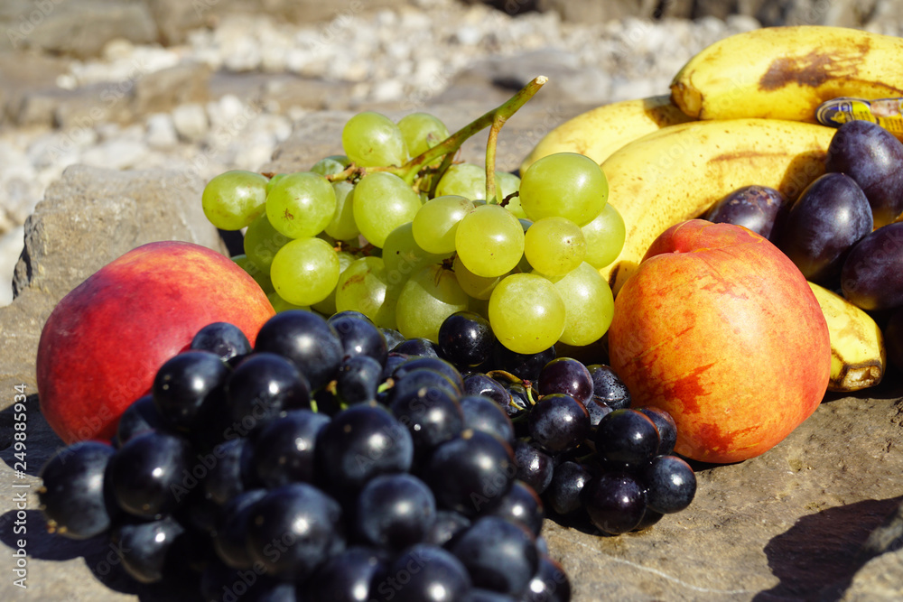 Assorted summer fruits laid out for a picnic on a rocky beach. Assorted summer fruits laid out for a picnic on a rocky beach.