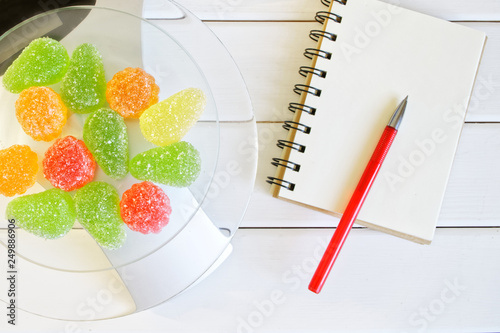 Multicolored marmalade on kitchen scales next to a notebook and a fountain pen. Counting and recording the amount of protein, calories and fat in food photo