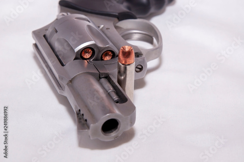 A stainless 357 magnum revolver with a single bullet next to it shown on a white background photo