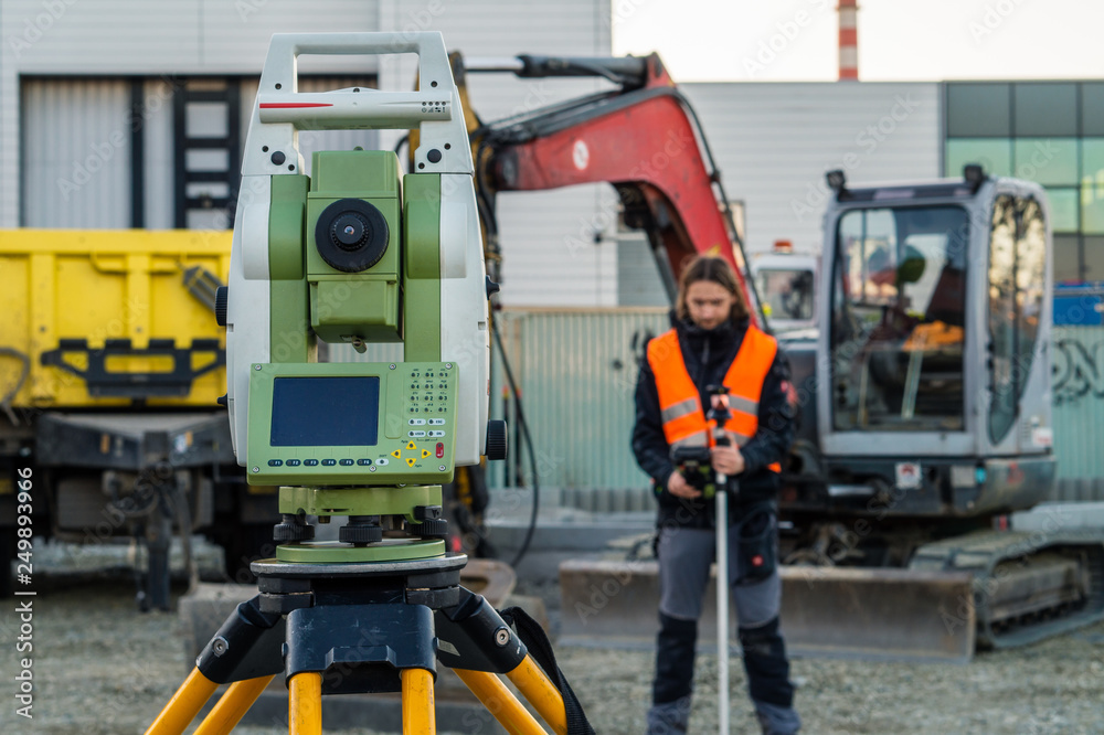Surveyor engineer with equipment (theodolite or total positioning station) on the construction site of the road with construction machinery background 