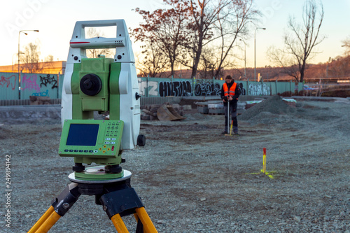 Surveyor engineer with equipment (theodolit or total positioning station) on the construction site of the road with construction machinery background 