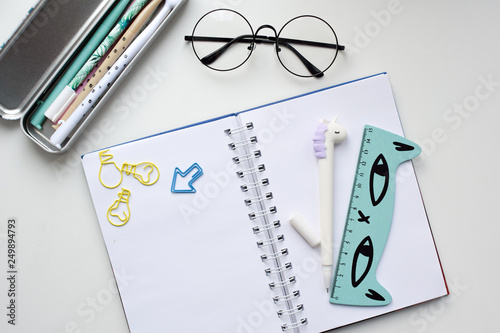 Top view of an open blank notebook with a pen in the form of a unicorn, a pencil case with kawaii pens