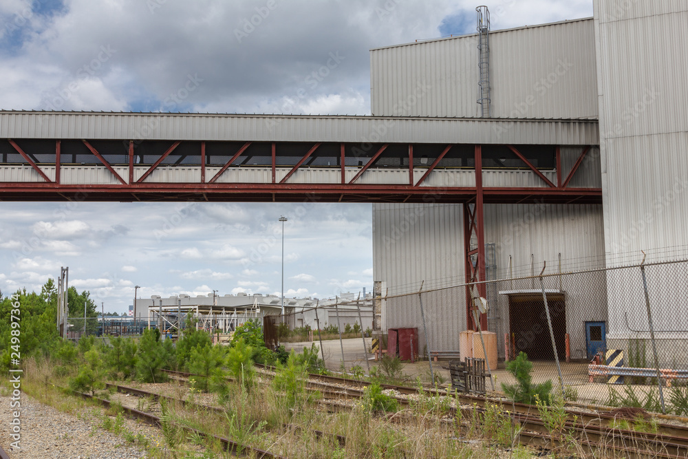 Walkway over grass filled train tracks into abandoned car factory Walkway over grass filled train tracks into abandoned car factory