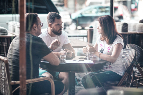 Businessmen discuss the deal and control it online, in a cafe on the street. A girl and two guys.