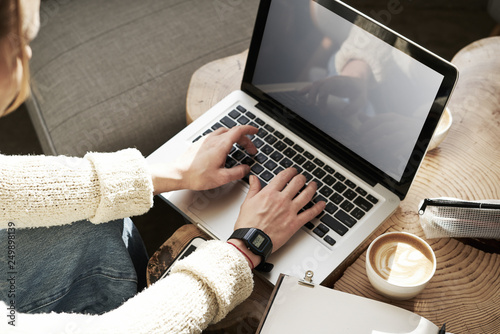 Close-up of woman's hands working on laptop, screen space for design layout. Woman having coffee at modern cafe, wooden slab table, sunshine.