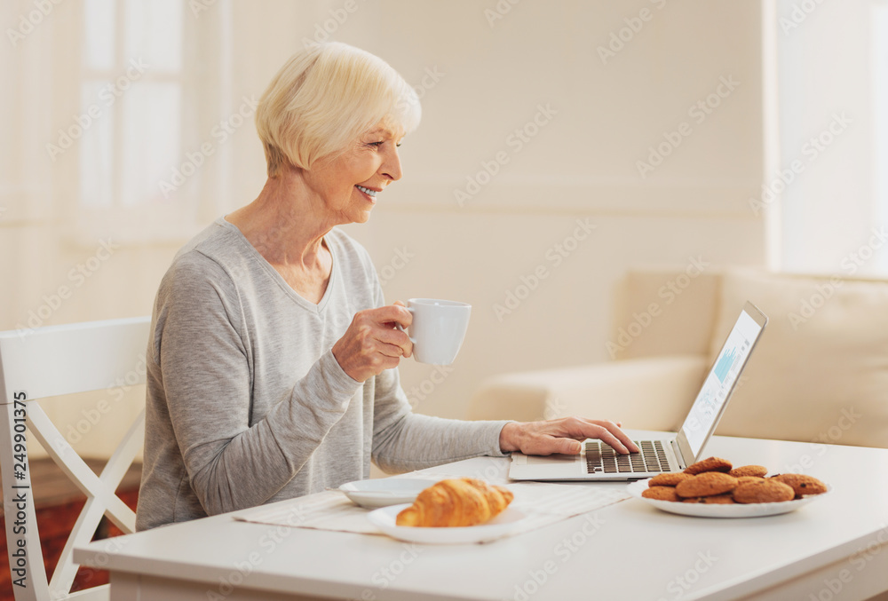 Woman checking e-mail while drinking tea in the kitchen Woman checking e-mail while drinking tea in the kitchen