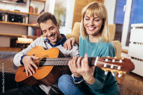 Romantic couple having fun at home, man playing guitar