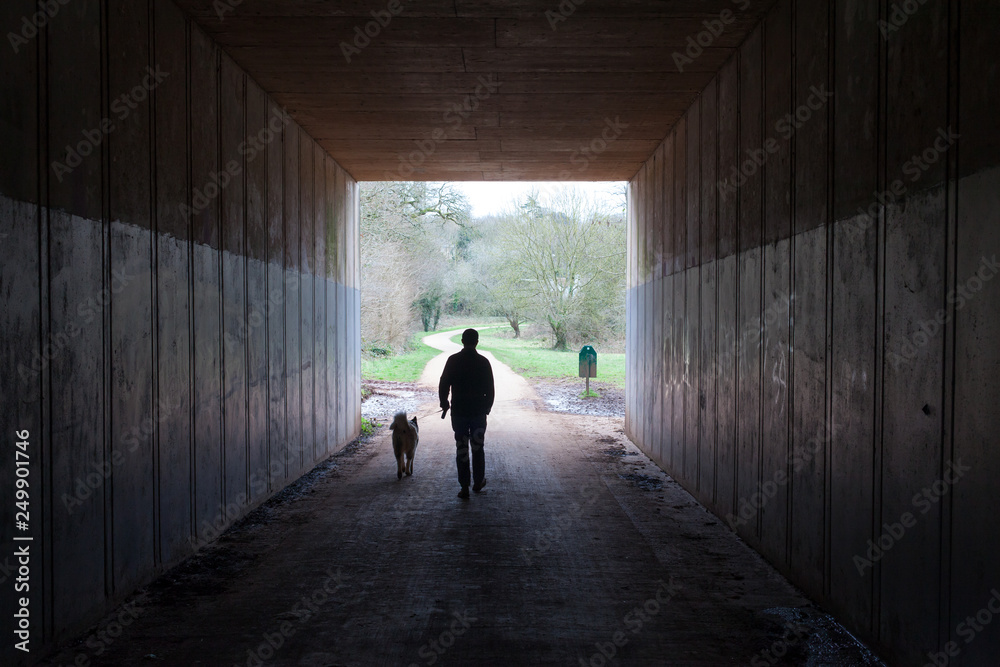 A man and his dog walking out of a tunnel into a bright green park A man and his dog walking out of a tunnel into a bright green park