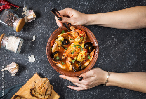 French fish soup Bouillabaisse with seafood, salmon fillet, shrimp, mussels. Female hands hold spoon photo