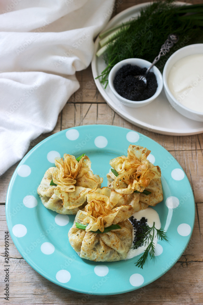 Bags of pancakes stuffed with herring, served with caviar, sour cream and dill on a wooden background. Rustic style. Bags of pancakes stuffed with herring, served with caviar, sour cream and dill on a wooden background. Rustic style.