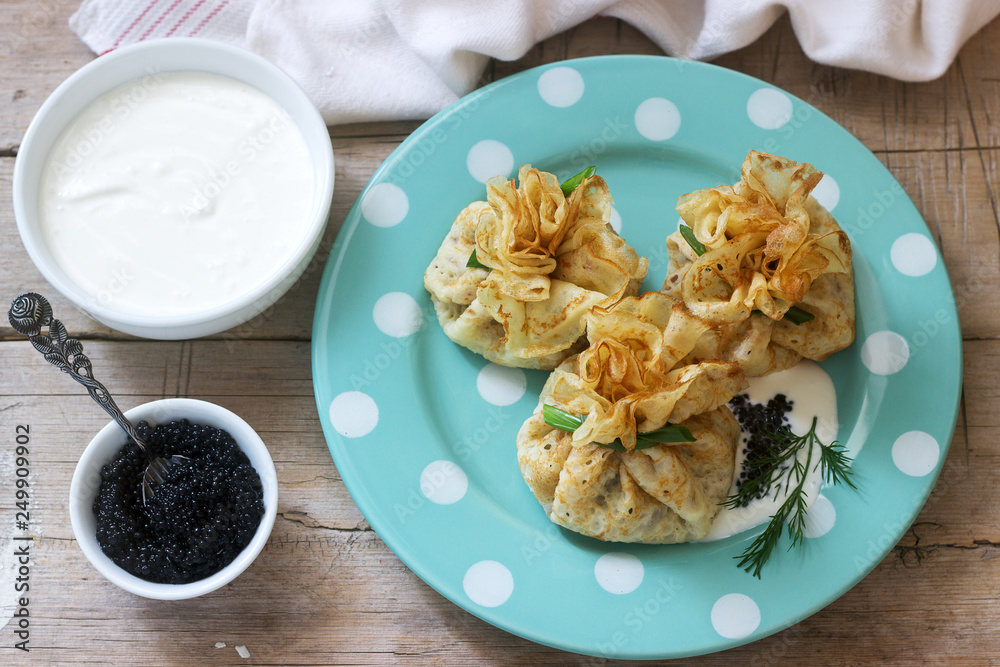 Bags of pancakes stuffed with herring, served with caviar, sour cream and dill on a wooden background. Rustic style.