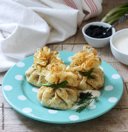 Bags of pancakes stuffed with herring, served with caviar, sour cream and dill on a wooden background. Rustic style. photo