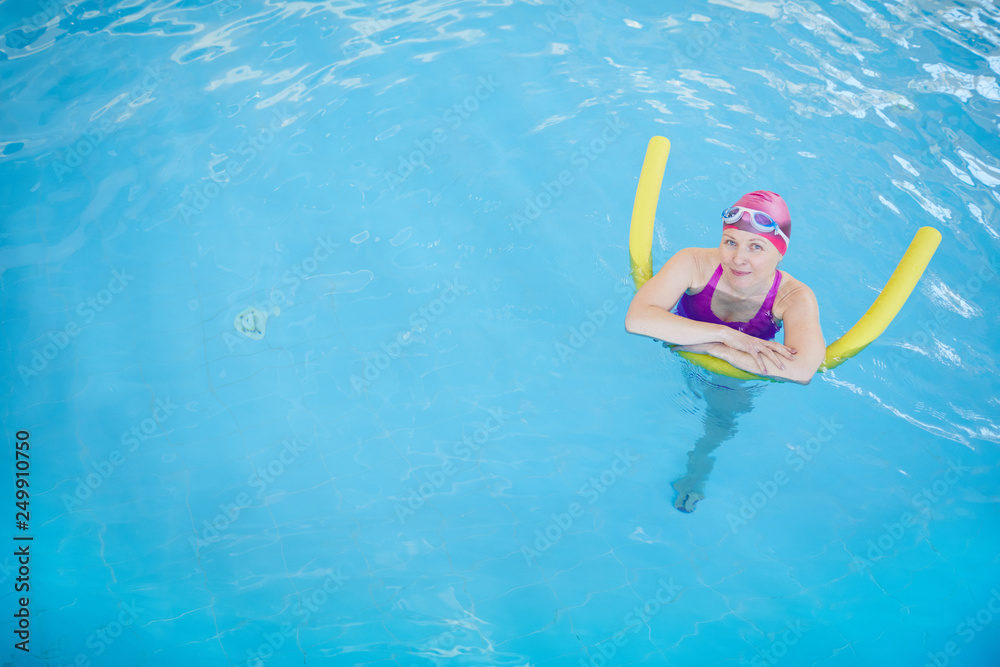 Top view portrait of happy senior woman swimming in pool and looking at camera, copy space