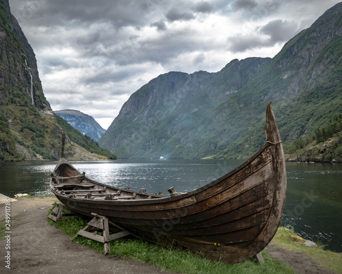 Traditional viking boat near fjord and mountains with dramatic cloudy sky.  photo